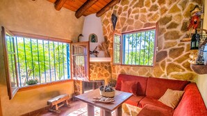 A cozy room with a stone wall, a red sofa, a wooden table with a basket, and large windows with metal bars. - Cubo's Jacaranda Rural Cottage / Private Pool / Views (Guaro)