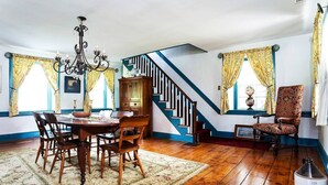 Un espace repas avec une table et des chaises en bois, un lustre et un escalier menant à l’étage supérieur.