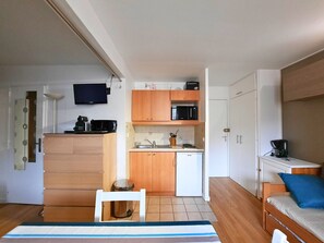 A compact room with a kitchenette, a bed with a blue pillow, and a small table.