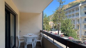 A balcony with a table and chairs, overlooking a street with buildings and trees. - Central studio with parking, 2 people. (Brides-les-Bains)