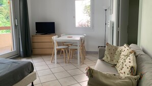 A room with a bed, a sofa, a dining table with chairs, a television, and a window with curtains. - Central studio with parking, 2 people. (Brides-les-Bains)