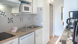Een moderne keuken met witte kastjes, een magnetron, een koffieapparaat en een spoelbak.