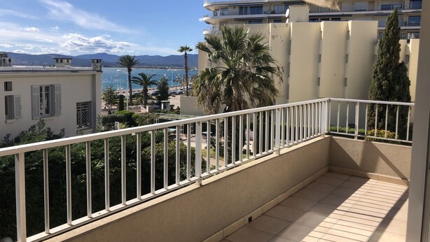 Een balkon met uitzicht op zee, palmbomen en een gebouw met balkons.