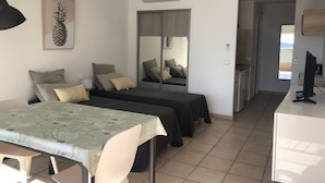 Een kleine kamer met een bed, een tafeltje en een stoel. Er is een spiegel, een raam en een airconditioning.