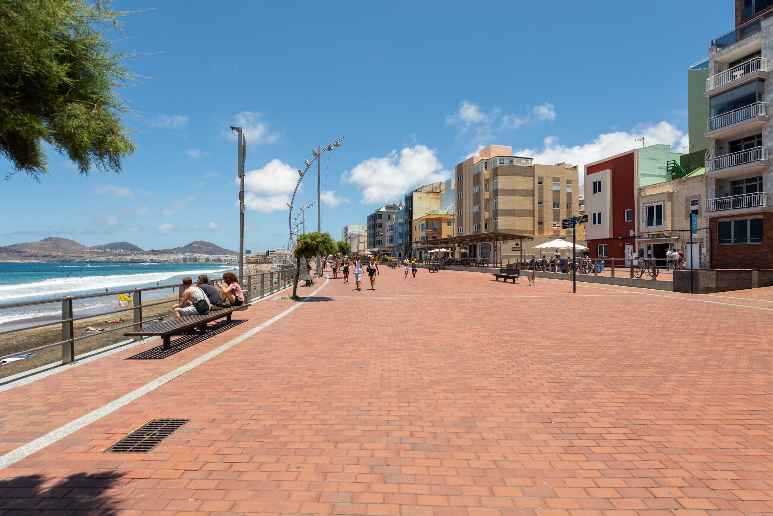 Un paseo marítimo con sendero pavimentado, bancos y vista al mar.