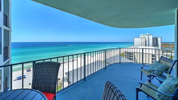 Un balcón con vista al océano y a la playa, muebles de mimbre y una mesa.
