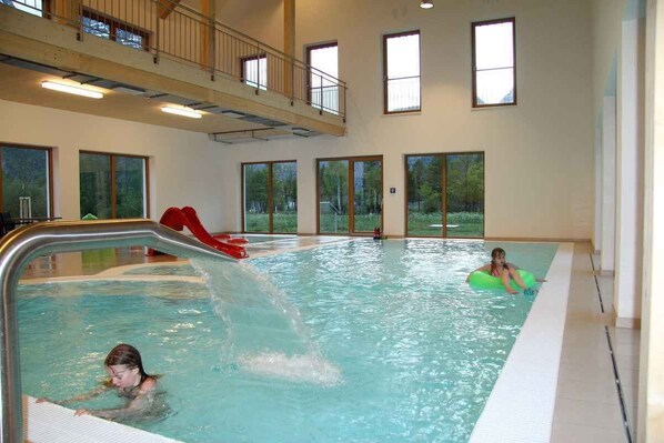 An indoor swimming pool with a slide, large windows, and a high ceiling.
