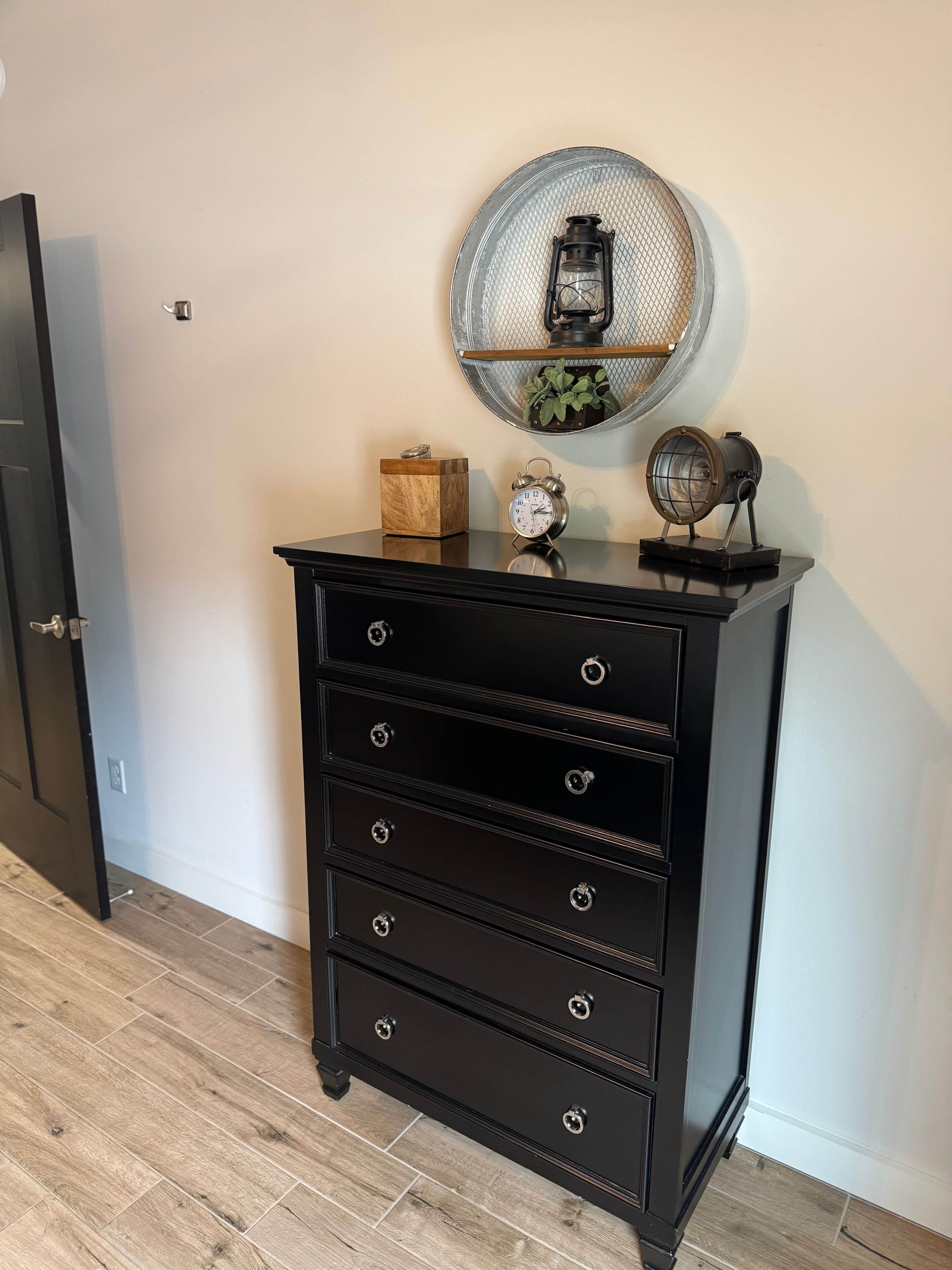 A black dresser with multiple drawers and a round mirror above it.