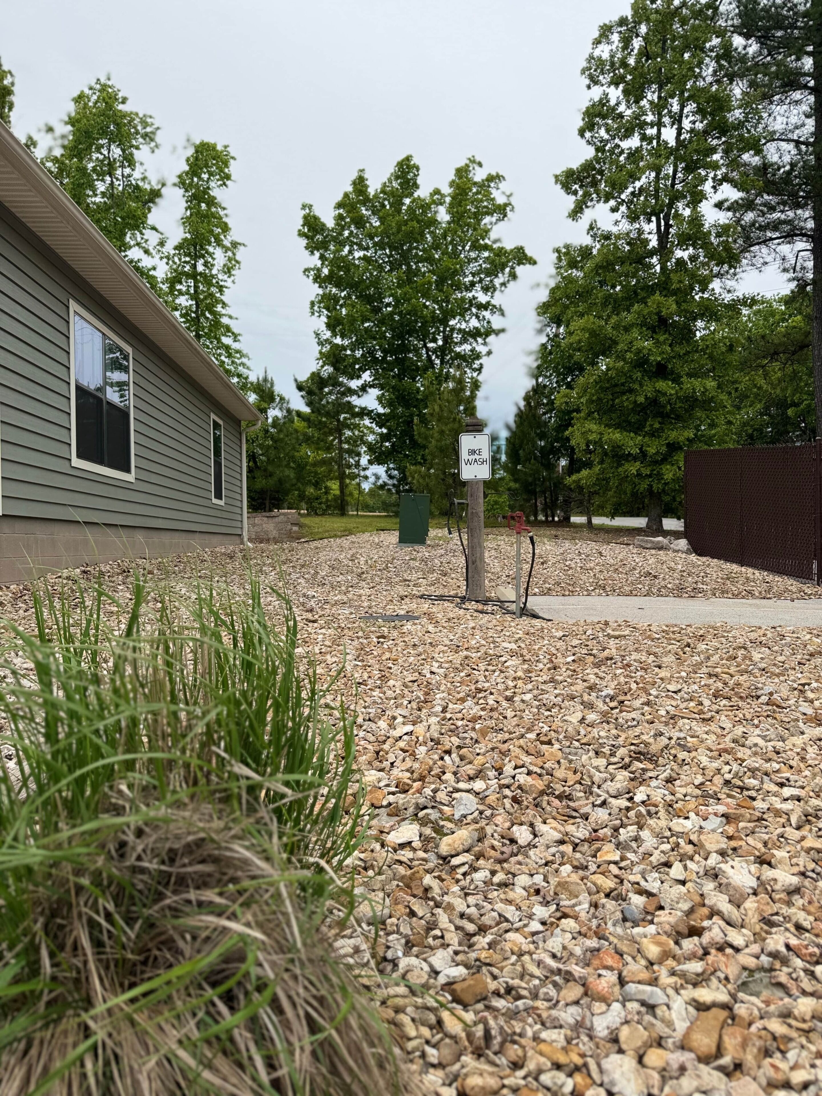 A gravel driveway leading to a building with a 'Bike Wash' sign, surrounded by trees and a fence.