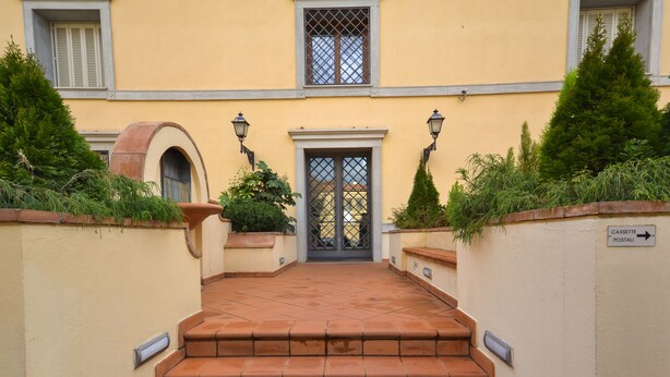 A building entrance with a tiled staircase leading to a door with a metal gate.