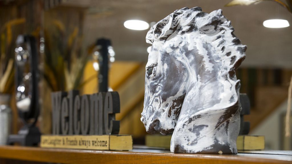 Eine Skulptur eines Löwenkopfes auf einem Sockel, im Hintergrund ein 'Welcome'-Schild.