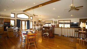 Una cocina amplia con armarios de madera, un comedor con sillas de madera, una barra y un televisor.