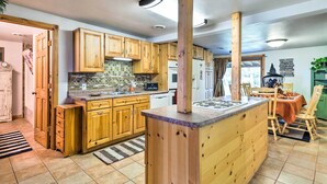 A kitchen with wooden cabinets, a central island, and a dining area with a table and chairs. - Family Home w/ Hot Tub - Walk to Johnson Lake! (Johnson Lake)