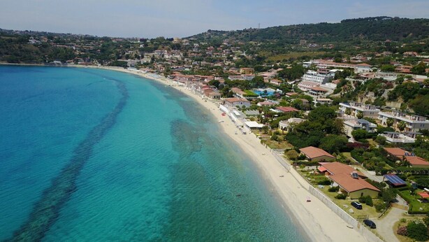 Vista aérea de un pueblo costero con una playa de arena, aguas turquesas cristalinas y edificios residenciales.