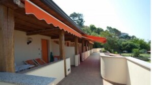 Un espacio al aire libre cubierto, con techo de madera y toldo rojo, que conduce a un edificio con puerta y ventanas.