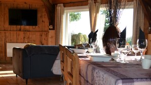 A dining area with a wooden table set for four, a sofa, and a television in a cabin-style room. - Gîte le Manège normand (Grand-Camp)