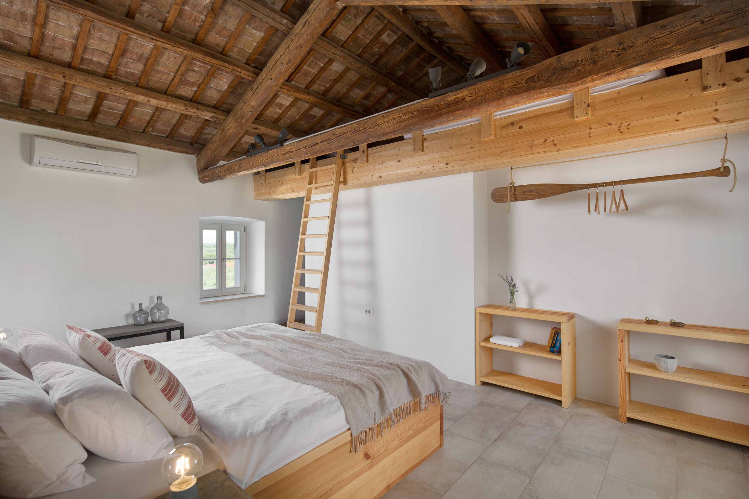 A bedroom with a wooden bed, a ladder, a shelf, and a window.
