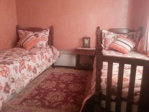 Un dormitorio con dos camas individuales, una silla de madera, una mesita de noche con un reloj y un radiador.
