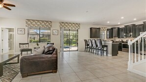 A spacious living area with a sofa, dining table, and chairs, a kitchen with dark cabinets, and a staircase. - EV_1447 - 6 Bed 6 Bath Villa with Screened Private Pool, Games Room, Kids Rooms (Davenport)