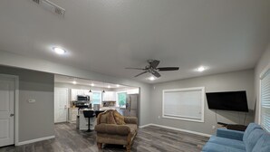 A spacious living area with a kitchen, a ceiling fan, and a flat-screen TV.