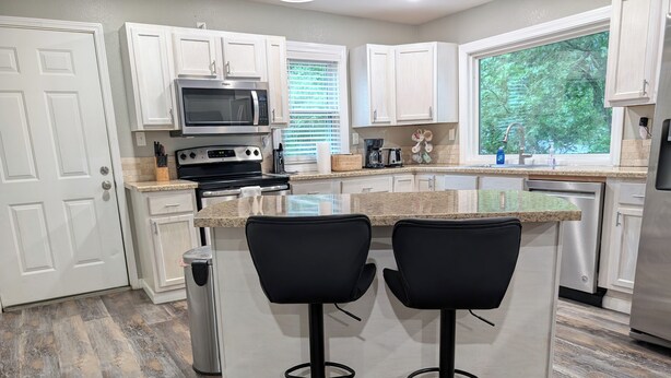 A modern kitchen with white cabinets, a microwave, a stove, a coffee maker, and a sink. There are two black bar stools at the island.