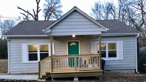 A single-story house with a front porch, a green door, and a small deck.