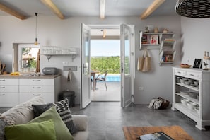 Una cocina moderna con armarios blancos, un comedor con mesa y sillas, y vista a una piscina a través de un ventanal.