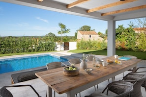 Una mesa de madera con sillas de mimbre, una piscina y vistas al campo.