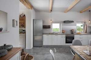 Una cocina moderna con armarios blancos, un refrigerador de acero inoxidable y un horno empotrado. Hay una ventana que ofrece luz natural y vistas al exterior.