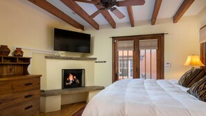 A bedroom with a fireplace, a TV mounted on the wall, a bed with a white duvet, wooden furniture, and a ceiling fan. - Short stroll to the historic plaza, Canyon Road & Railyard District Restaurants (Santa Fe)