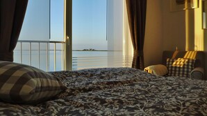 A bedroom with a large bed, a view of the sea through a sliding door, and a chair with a checkered cushion. - ⭐unique location at the beginning of the pier with unobstructed all-round water view⭐ (Kappeln/Ostseeresort Olpenitz)