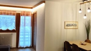 A cozy room with a wooden floor, a red sofa, a dining table with chairs, and a window with curtains. - Bright and Cozy Two-room apartment with balcony overlooking the Matterhorn (Breuil-Cervinia)