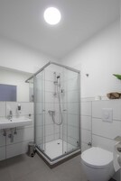 Un baño moderno con ducha envuelta en vidrio, un lavabo blanco y un inodoro.