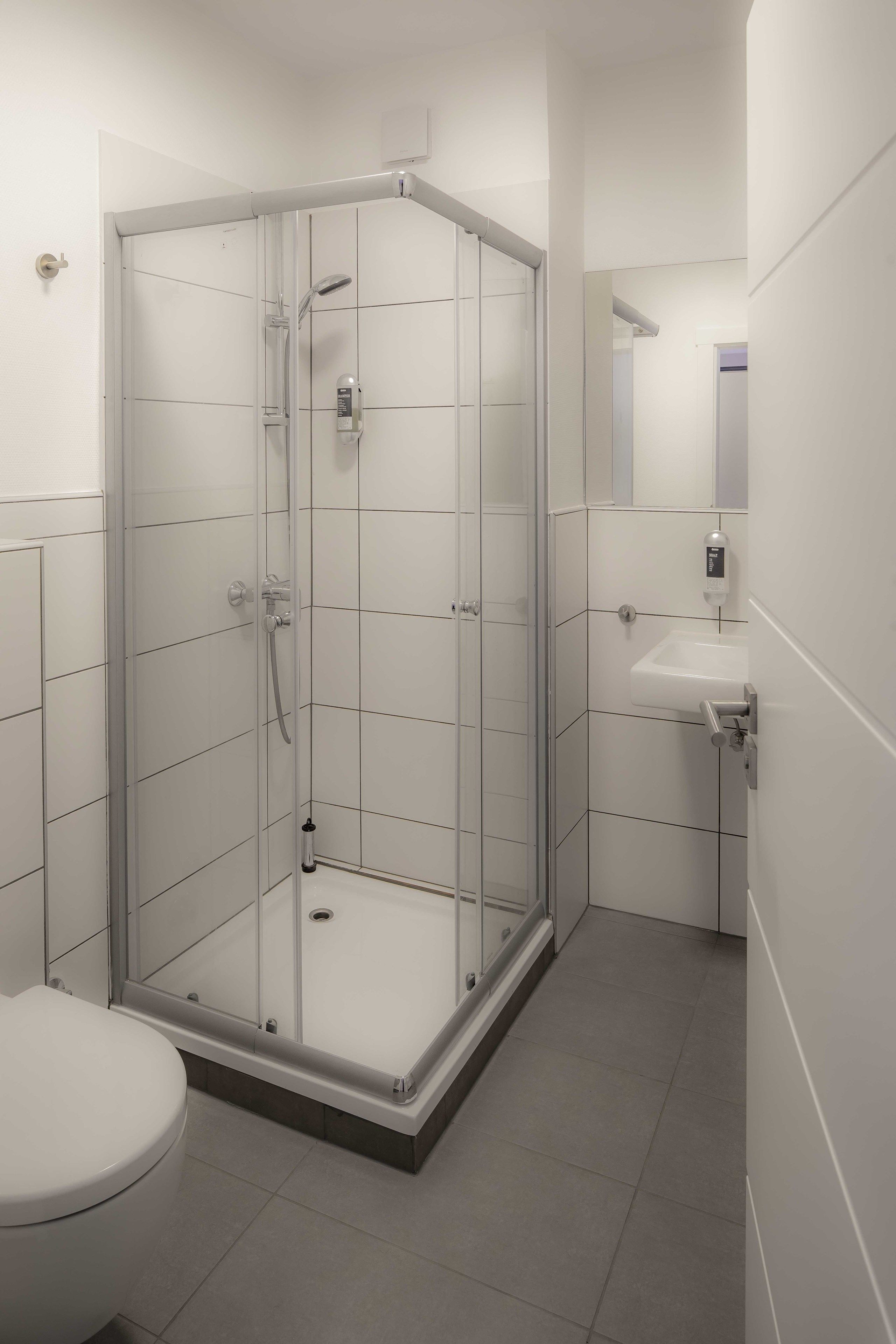 Een moderne badkamer met een douchecabine van glas, een wit wastafelmeubel en een toilet.