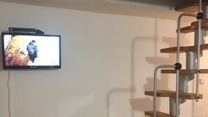 A staircase with wooden steps and metal railings, a television mounted on the wall, and two remote controls on a wooden table. - The Cottage with a big private garden (Keszthely)