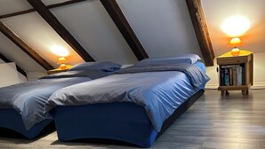 A bedroom with a loft-style ceiling, a bed with blue bedding, a small wooden nightstand with a lamp, and a patterned rug on the floor. - The Cottage with a big private garden (Keszthely)