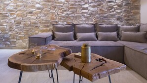 Een gezellige zithoek met een stenen muur, een grijze bank en twee houten salontafels met drankjes en een kaars.
