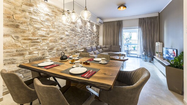 Een eetgedeelte met een stenen muur, een houten tafel gedekt voor vier personen, en een moderne bank op de achtergrond.