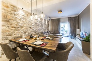 A dining area with a stone wall, a wooden table set for four, and a modern sofa in the background.