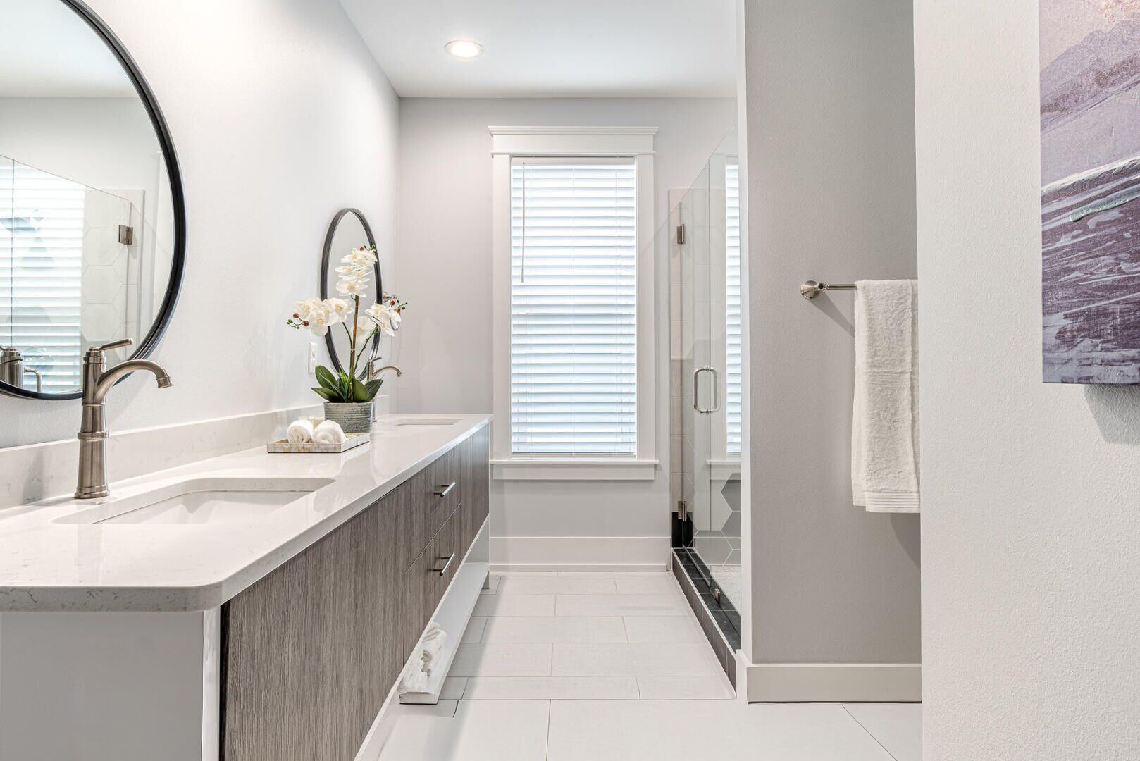 A modern bathroom with a double sink, a large mirror, and a shower area.