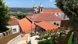 Vista de un edificio con techo de tejas rojas, una torre de campanas y una escalera que conduce a una entrada con portón.