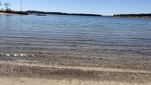 A calm lake with a sandy shore and a pier extending into the water. - Tree Top Lake Views with lake access for swimming fishing boating 250 ft away! (Pottsboro)