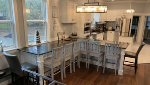 A modern kitchen with white cabinetry, a central island with bar stools, and a hanging light fixture. - Tree Top Lake Views with lake access for swimming fishing boating 250 ft away! (Pottsboro)