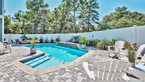 A swimming pool with a stone deck, surrounded by white chairs and potted plants.