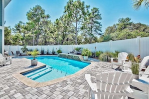 A swimming pool with a stone deck, surrounded by white chairs and potted plants.