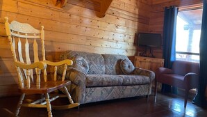 A wooden cabin interior with a sofa, rocking chair, and a television. - Cozy Cabin with Fire Pit pavilion near boat ramp (Broken Bow)