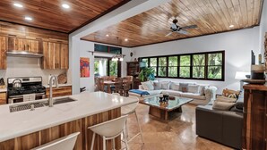 Amplia sala de estar con un ventanal grande, una cocina con armarios de madera y un ventilador de techo.