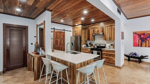 Una cocina moderna con armarios de madera, una isla central con taburetes altos y un refrigerador de acero inoxidable.