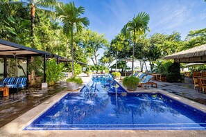 A pool area with lounge chairs, a covered seating area, and tropical vegetation.