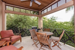 An outdoor patio with a wooden table and chairs, a grill, and a ceiling fan.